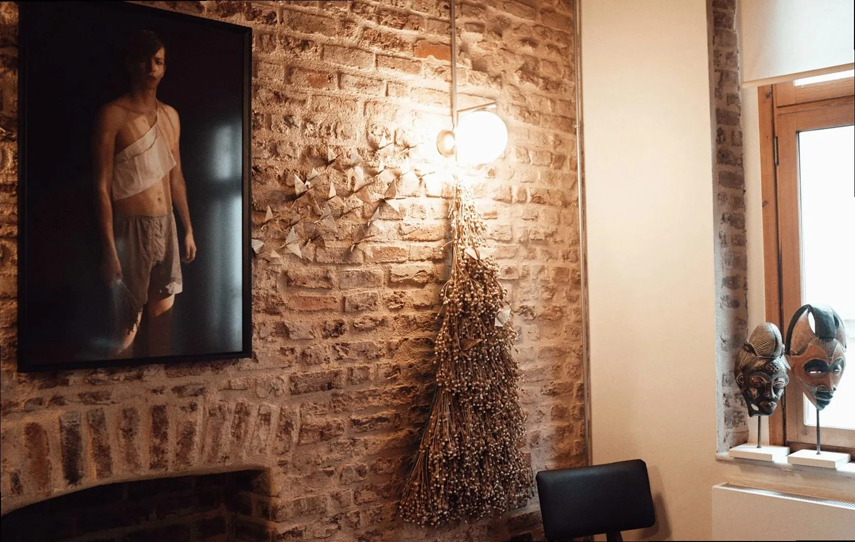 Interior of light cafe with brick wall decorated with picture of man near lamp and hanging garland with dry herbs near c